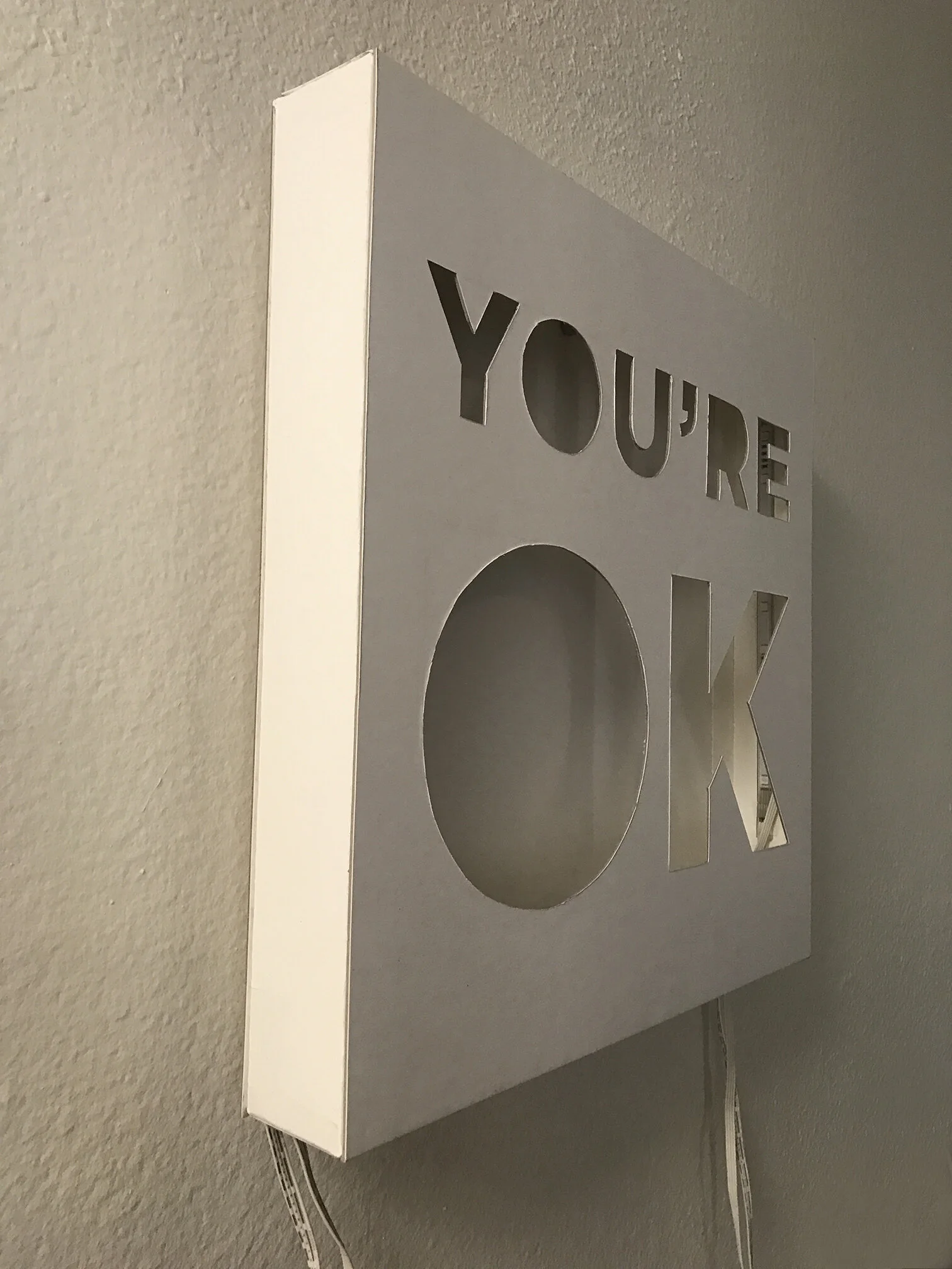 You're OK — side view of hand-cut cardstock letters lit by LEDs
